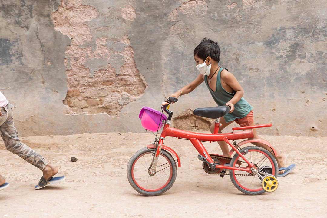 A young boy wearing a mask pushing his bicycle on a street in Rajasthan, India. Credit: Benedikt V. Loebell.