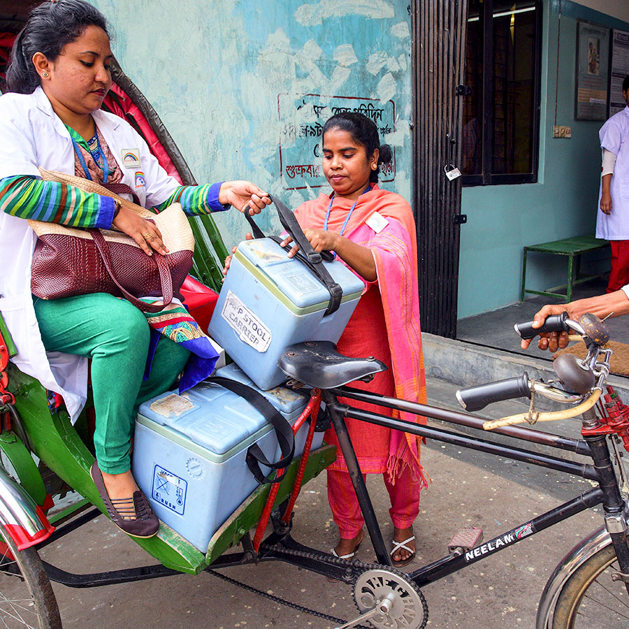 Muna, a Community Health Care Provider is carrying the vaccines by Rickshaw to the distribution point