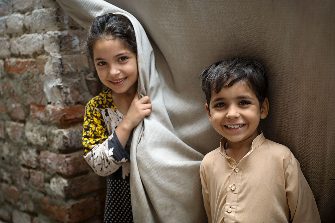 Parkha (10) with her brother Asif (5) stand outsider their house observing health worker during the door-to-door polio campaign in Rasheed Garhi, Peshawar city, Khyber-Pakhtunkhwa province, Pakistan. Credit: Asad Zaidi/Gavi/2023