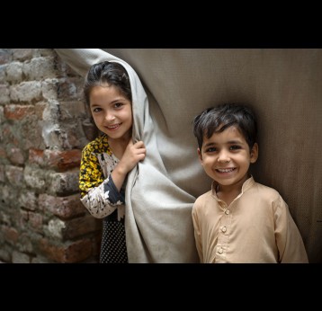 Parkha (10 ans) et son frère Asif (5 ans) se tiennent à l'extérieur de leur maison pour observer un agent de santé pendant la campagne de porte-à-porte contre la poliomyélite à Rasheed Garhi, dans la ville de Peshawar, dans la province de Khyber-Pakhtunkhwa, au Pakistan. Crédit : Asad Zaidi/Gavi/2023