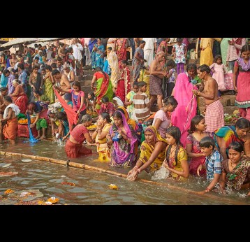 A crowd in a sacred ritual bath in a Ganges River ghat at dawn.
