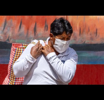 Man in respiratory mask during coronavirus pandemic in market with bag of food in Cusco, Peru