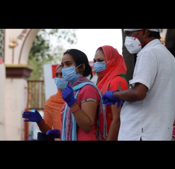 Indian health workers wearing personal protective equipment (PPE) and relatives carrying the mortal remains of a COVID-19 victim at the cremation ground