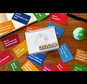 A table with a card with the SDG goals and a ball of earth, a small sketchbook with SDG symbols and a wooden cube stamped with the letters SDGs.