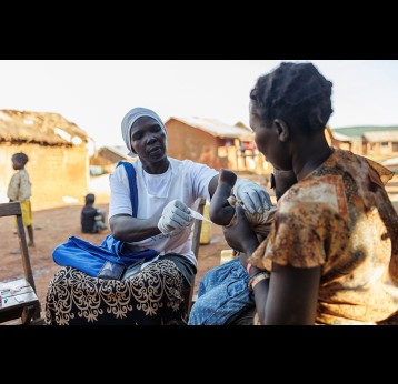 Mutesi Fatuma prend la température de l'enfant de Wanga Glady. Fatuma a été formée pour effectuer des évaluations du paludisme et distribuer des médicaments aux enfants de moins de cinq ans. Living Goods/2022/Jjumba Martin.