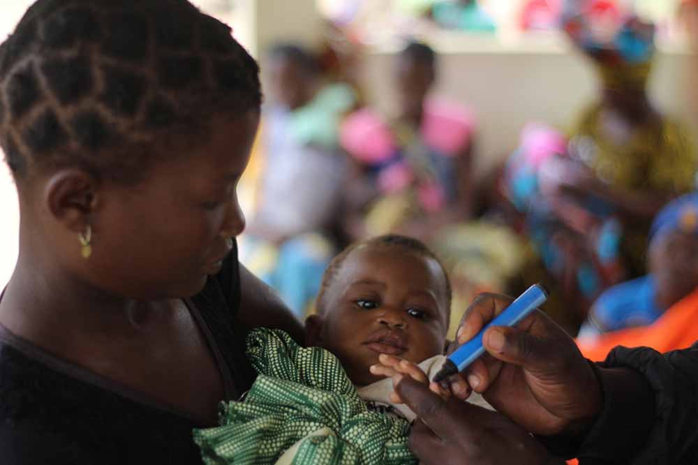 A mother holds her child, whose finger is being marked to show that the child received a polio vaccine on April 28, 2022. Credit: ©UNICEF/UN0632380/Lemos