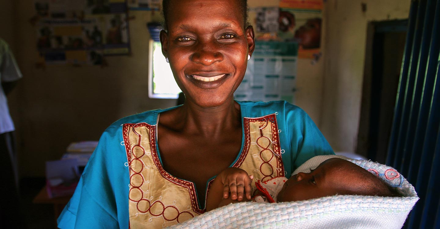 GAVI/2014/Mike Pflanz/South Sudan - A woman smiles into the camera holding her baby during the pentavalent vaccine introduction in South Sudan