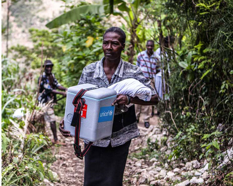 health worker helps carry cold chain equipment in Haiti. Credit: Gavi/2013/Evelyn Hockstein