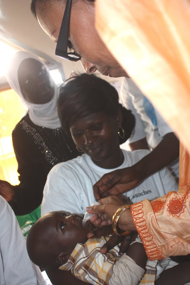 Health minister Bouy  delivers the 'new' vaccine herself to one of the children waiting in line -- the latest of 11 life-saving vaccines that The Gambia provides for all children.