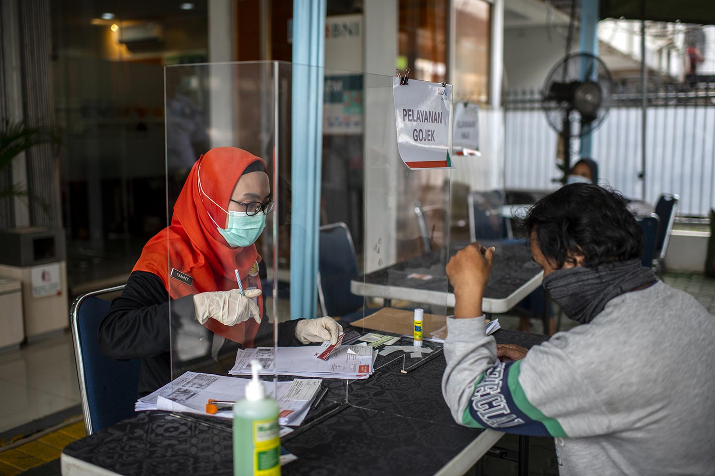 Bank officer (left) serving to customer in front of the bank using protective glass during Covid-19 outbreak in South Jakarta, Indonesia on 31 March, 2020. Almost all bank in Jakarta implement a social distancing for customer services. Credit: UNICEF/2020/Arimacs Wilander