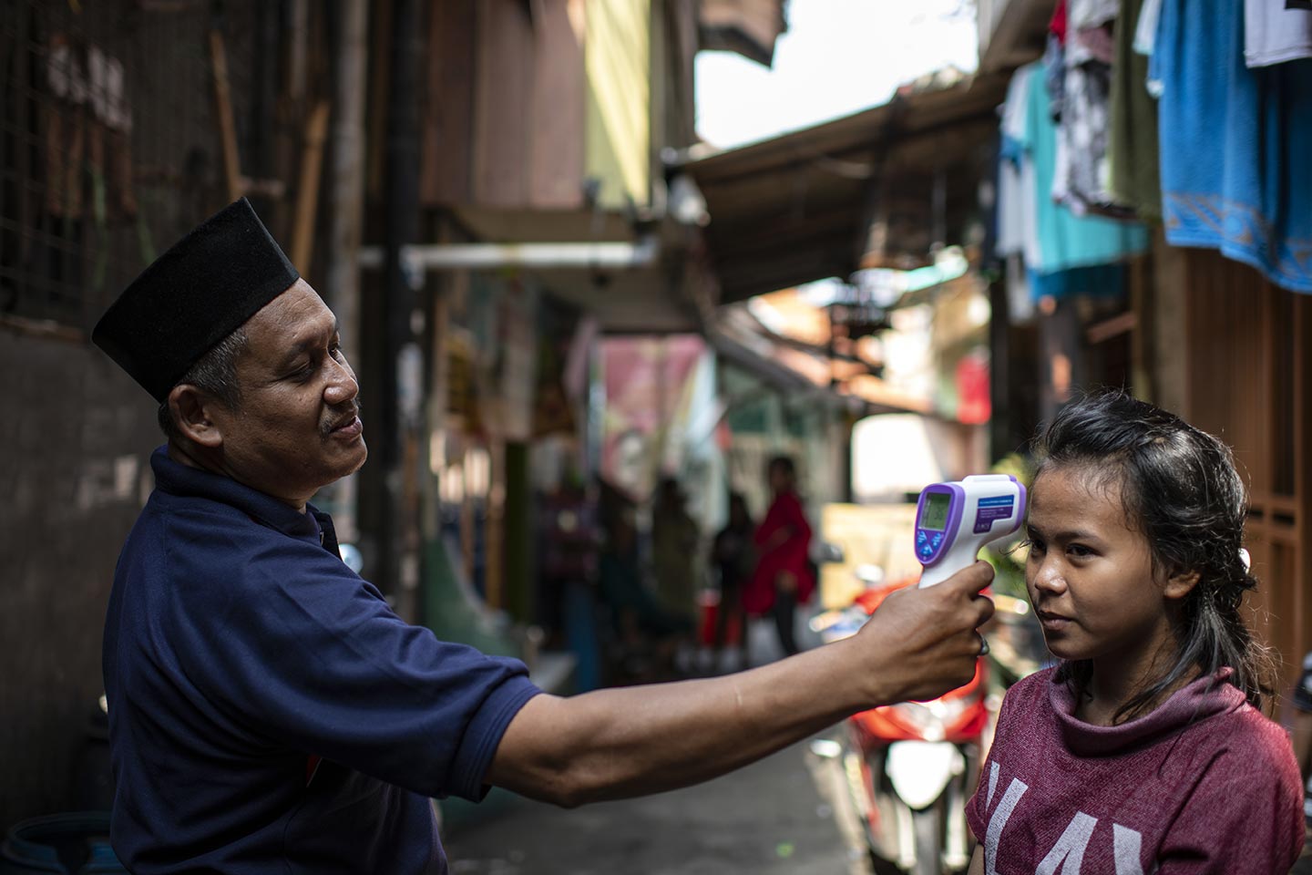 Sudirman, 55, head of RT (left) is checking Zahra temperature during the Covid-19 outbreak in slum area in West Jakarta, Indonesia on 1 April, 2020. Credit: UNICEF/2020/Arimacs Wilander
