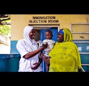 Two health workers holding a baby in front of Immunisation injection room- GAVI/2013/Adrian Brooks