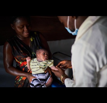 A masked health worker vaccinates an infant in Nigeria. Credit: Gavi/2021/Christophe Da Silva