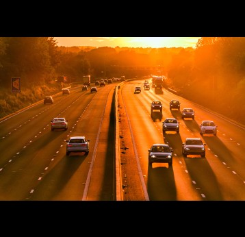 Burning hot sunset on uk motorway with long shadows of moving car traffic in england