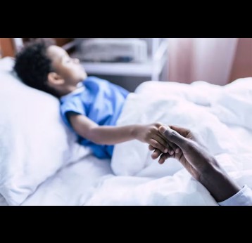 A hand holding the hand of a child in a hospital bed. Credit: LightField Studios/Shutterstock