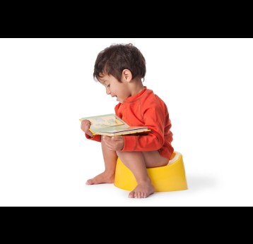 Small boy reading a book while sitting on the potty.