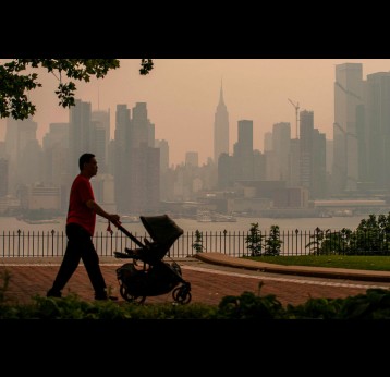 A person walks with a stroller in a park in front of the New York City skyline in June 2023 as it’s covered with haze and smoke from Canada wildfires. Visual: Eduardo Munoz Alvarez/Getty Images