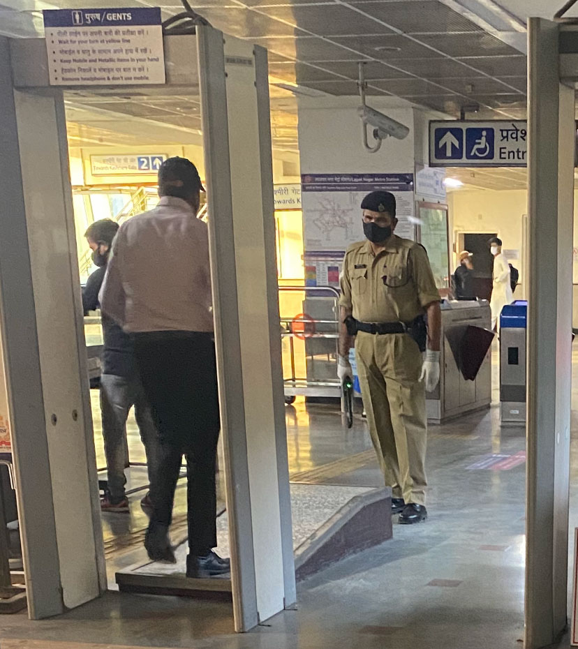 A Delhi Metro guard wearing mask and gloves, checking on commuters.
