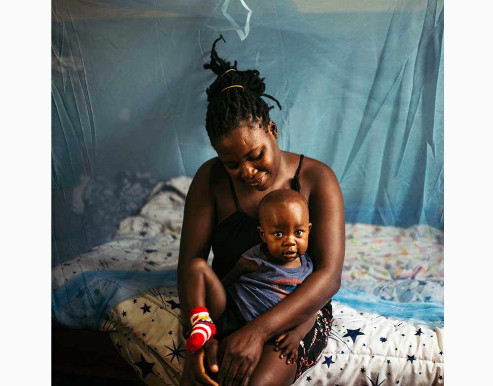 In Nyalenda B, an informal settlement in Kisumu, western Kenya, a woman with her son on their bed with government-issued mosquito nets.