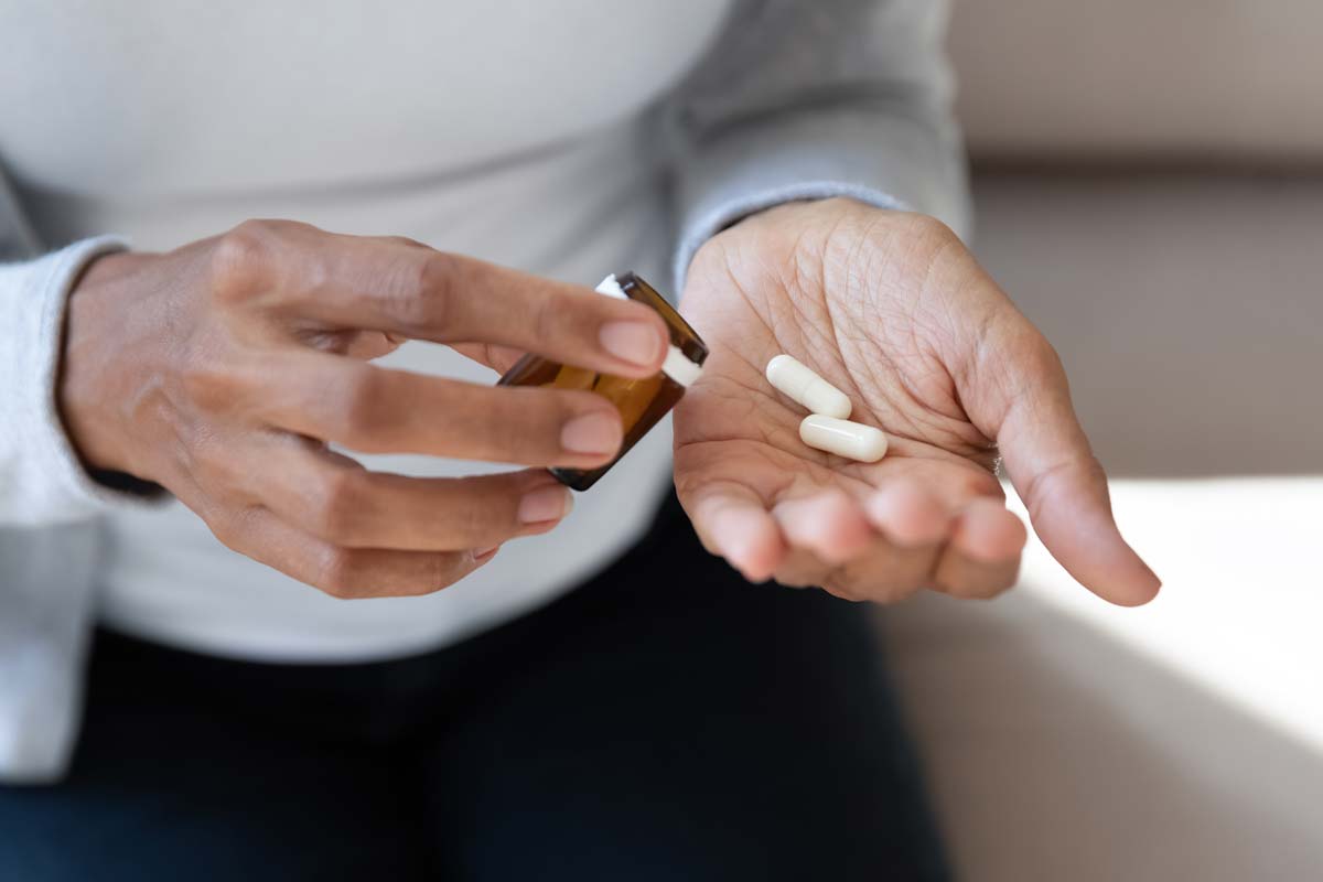 A woman holding white pill capsules in her hand.