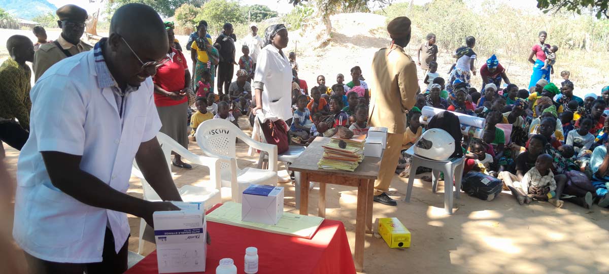 A village leader explains the importance of vaccines to his community as a health worker prepares vaccines to administer to children. Credit: Charles Mangwiro.