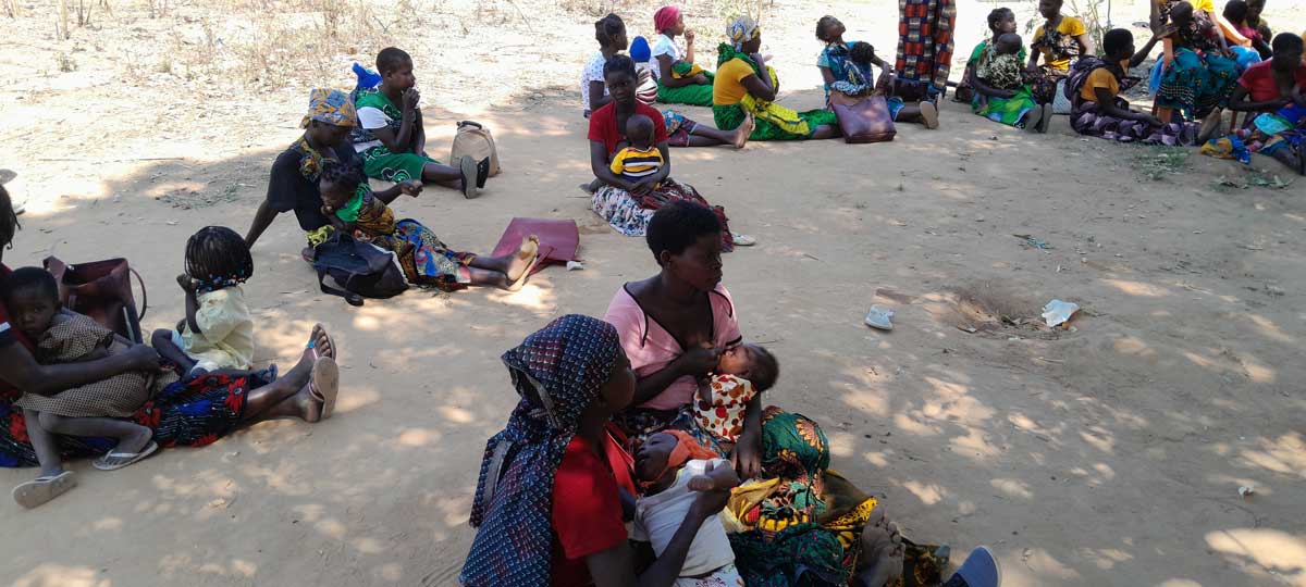 Women sitting under a tree with their kids, awaiting their turn to receive the malaria vaccine. Credit: Charles Mangwiro